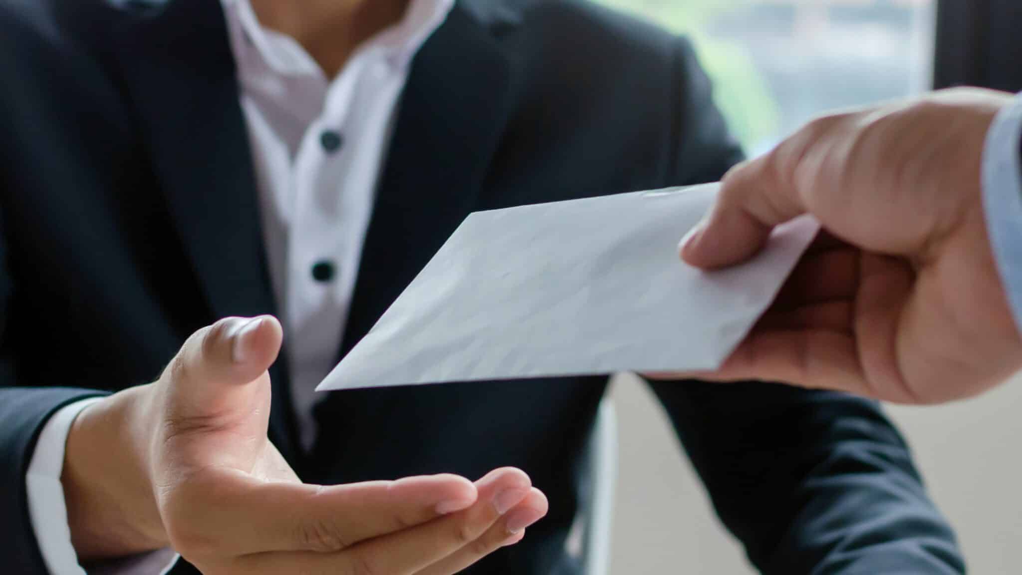 Ein Mitarbeiter im dunkelblauen Anzug reicht ein Blatt Papier weiter, während im Hintergrund das Büro unscharf bleibt – AHW Krisenbonus.